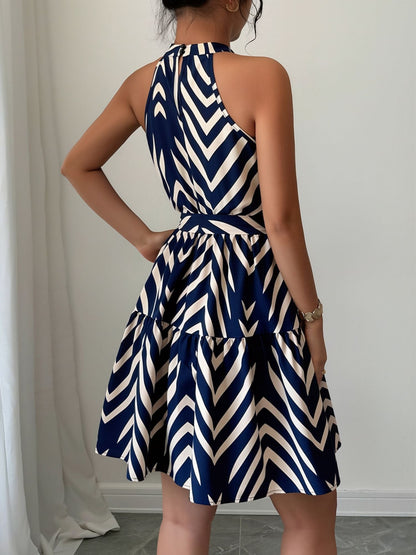 Blue - Woman wearing a geometric patterned halter-neck mini dress with a tie waist and tiered skirt.