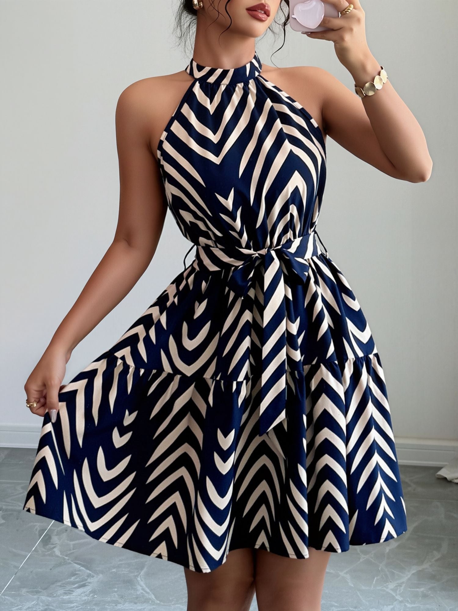 Blue - Woman wearing a geometric patterned halter-neck mini dress with a tie waist and tiered skirt.