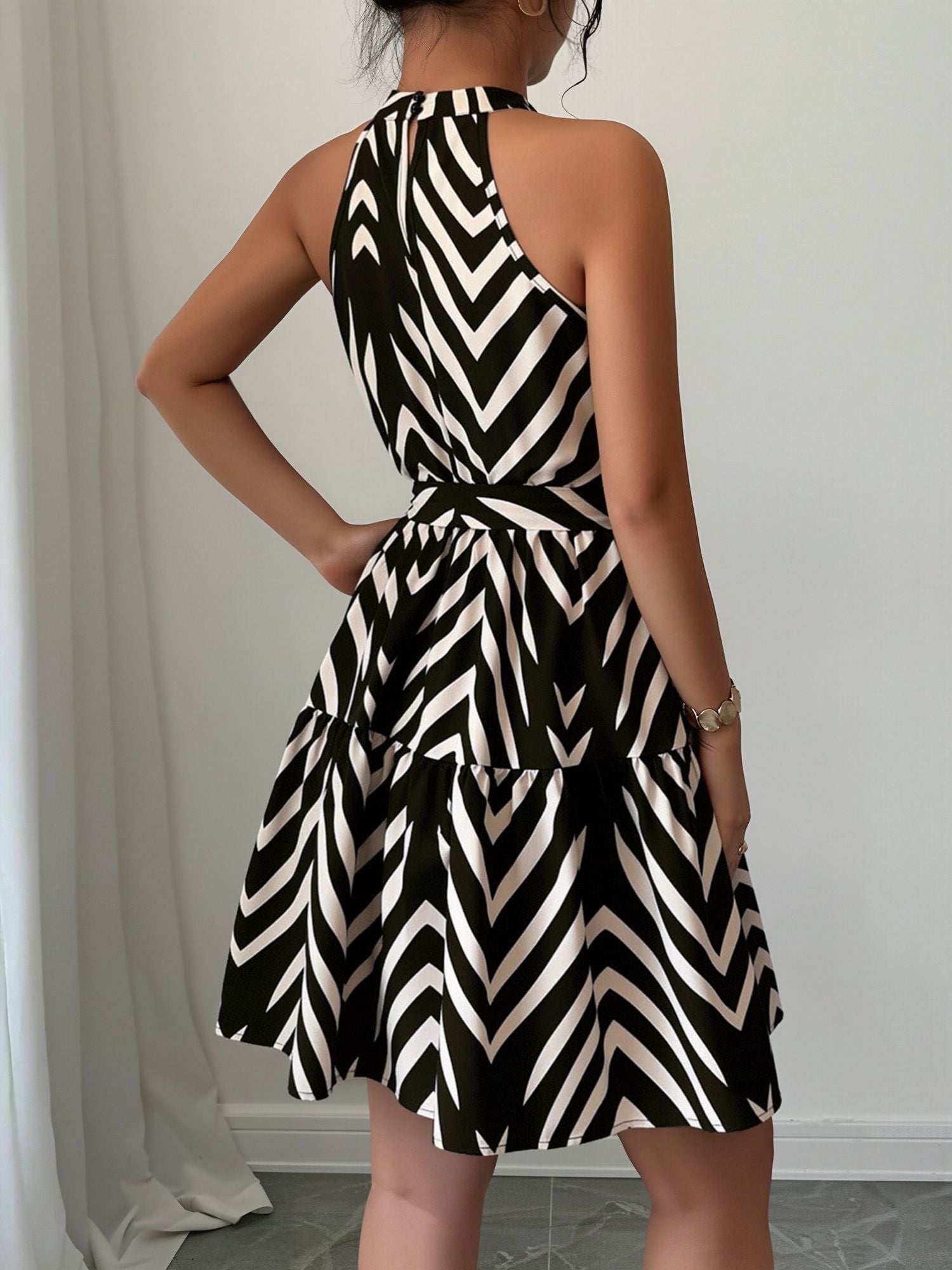 Black - Woman wearing a geometric patterned halter-neck mini dress with a tie waist and tiered skirt.