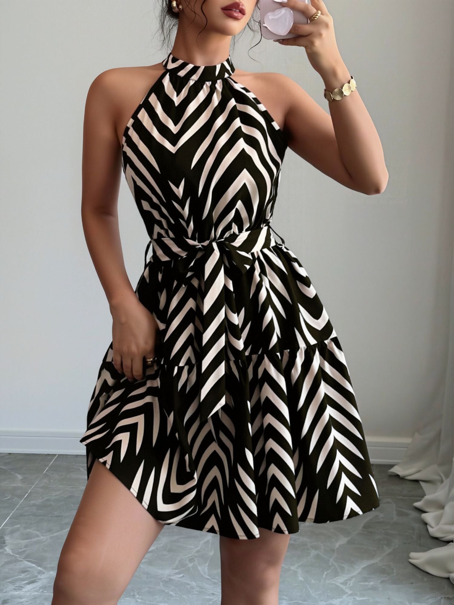 Black - Woman wearing a geometric patterned halter-neck mini dress with a tie waist and tiered skirt.