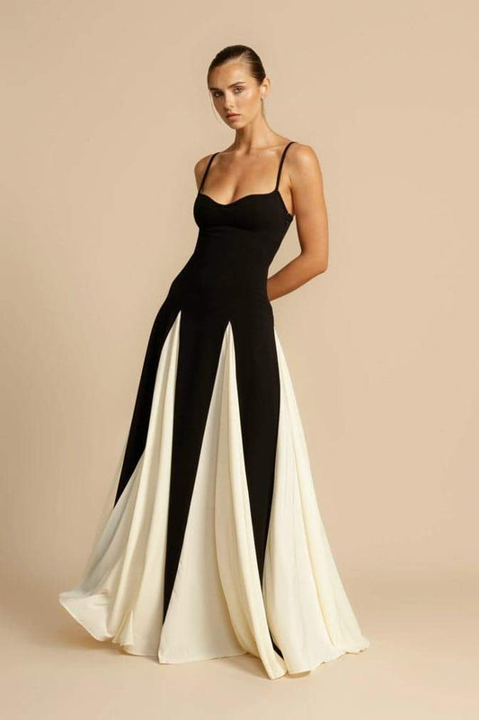 Black - A woman models a floor-length, two-tone maxi dress featuring a fitted dark bodice with spaghetti straps and a voluminous skirt constructed with alternating dark and flowing light godet panels.