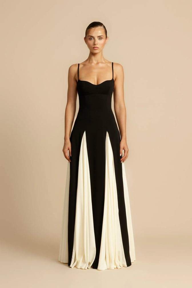 Black - A woman models a floor-length, two-tone maxi dress featuring a fitted dark bodice with spaghetti straps and a voluminous skirt constructed with alternating dark and flowing light godet panels.