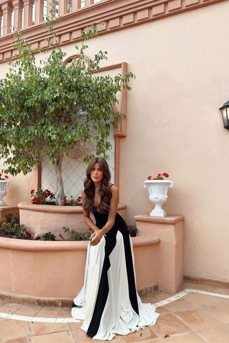 Black - A woman models a floor-length, two-tone maxi dress featuring a fitted dark bodice with spaghetti straps and a voluminous skirt constructed with alternating dark and flowing light godet panels.