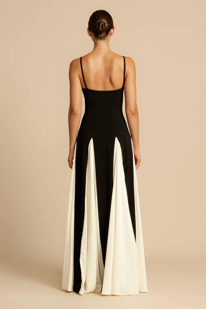 Black - A woman models a floor-length, two-tone maxi dress featuring a fitted dark bodice with spaghetti straps and a voluminous skirt constructed with alternating dark and flowing light godet panels.