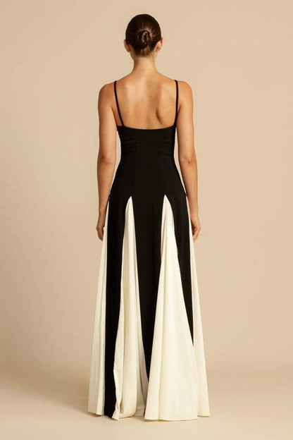 Black - A woman models a floor-length, two-tone maxi dress featuring a fitted dark bodice with spaghetti straps and a voluminous skirt constructed with alternating dark and flowing light godet panels.