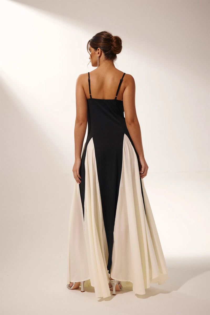 Black - A woman models a floor-length, two-tone maxi dress featuring a fitted dark bodice with spaghetti straps and a voluminous skirt constructed with alternating dark and flowing light godet panels.