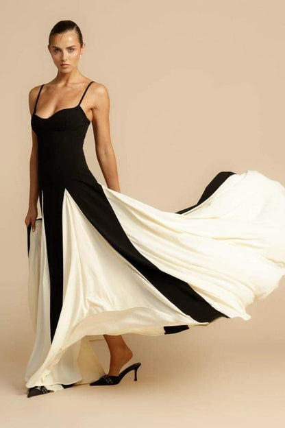 Black - A woman models a floor-length, two-tone maxi dress featuring a fitted dark bodice with spaghetti straps and a voluminous skirt constructed with alternating dark and flowing light godet panels.