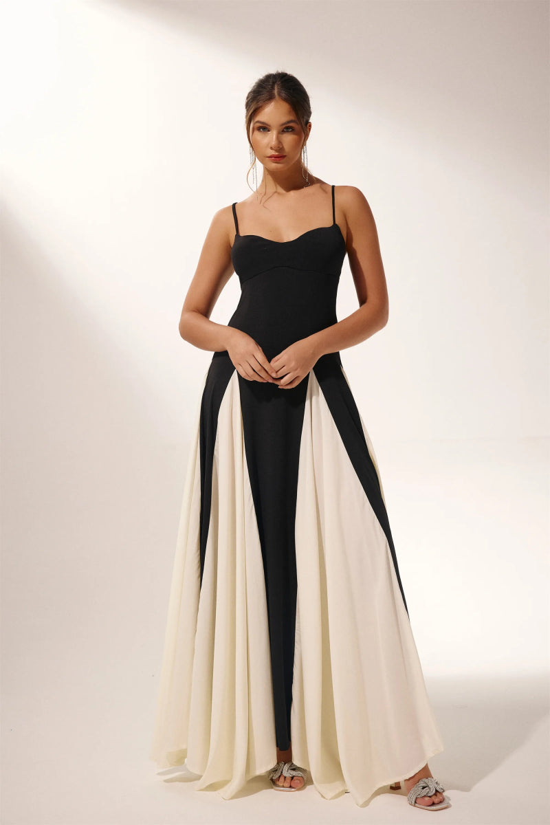 Black - A woman models a floor-length, two-tone maxi dress featuring a fitted dark bodice with spaghetti straps and a voluminous skirt constructed with alternating dark and flowing light godet panels.