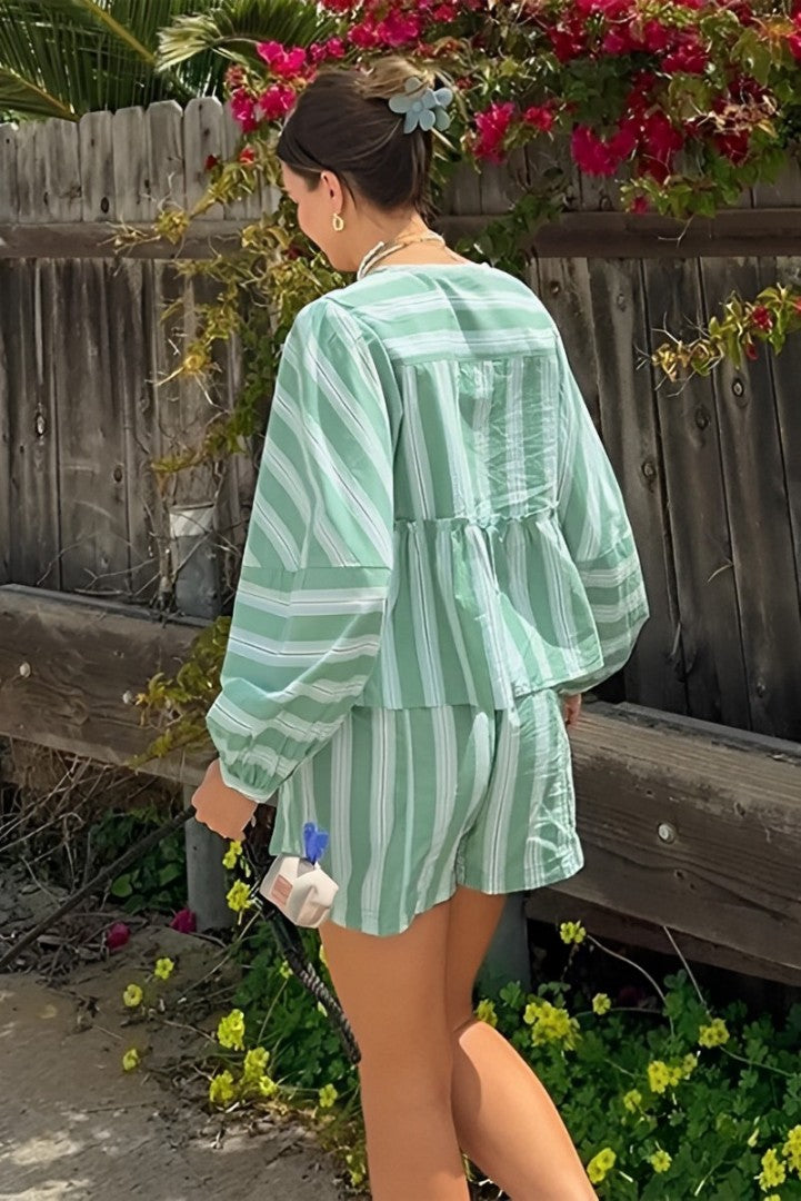Green - A woman wearing a relaxed-fit, green and white vertically striped two-piece set featuring a tiered peplum top with long balloon sleeves and a tie-front closure, paired with matching loose shorts, standing outdoors.