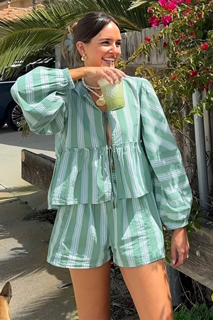 Green - A woman wearing a relaxed-fit, green and white vertically striped two-piece set featuring a tiered peplum top with long balloon sleeves and a tie-front closure, paired with matching loose shorts, standing outdoors.