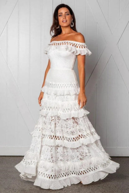 White - Woman wearing a white, off-the-shoulder maxi dress with tiered ruffles, lace, and broderie anglaise detailing.