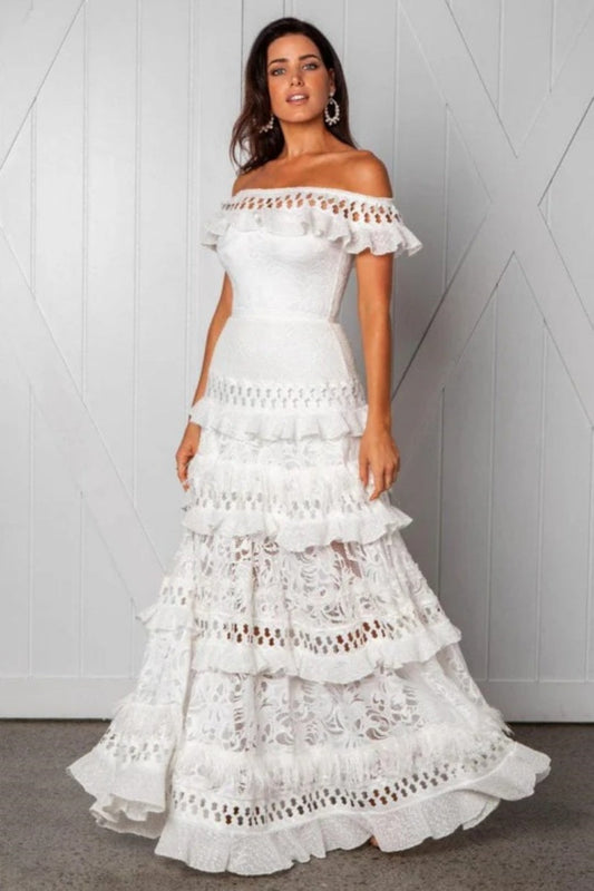 White - Woman wearing a white, off-the-shoulder maxi dress with tiered ruffles, lace, and broderie anglaise detailing.