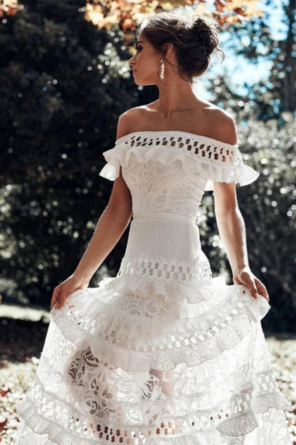 White - Woman wearing a white, off-the-shoulder maxi dress with tiered ruffles, lace, and broderie anglaise detailing.