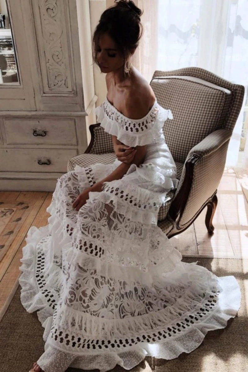 White - Woman wearing a white, off-the-shoulder maxi dress with tiered ruffles, lace, and broderie anglaise detailing.