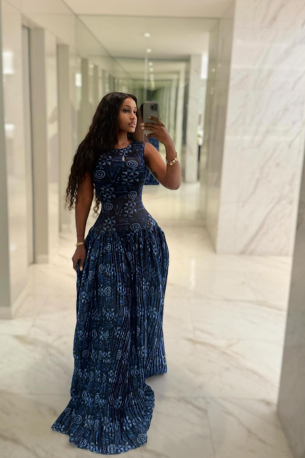 Blue - A woman wearing a sleeveless maxi dress featuring a fitted, semi-sheer geometric bodice and a voluminous gathered skirt with a mixed abstract blue print.