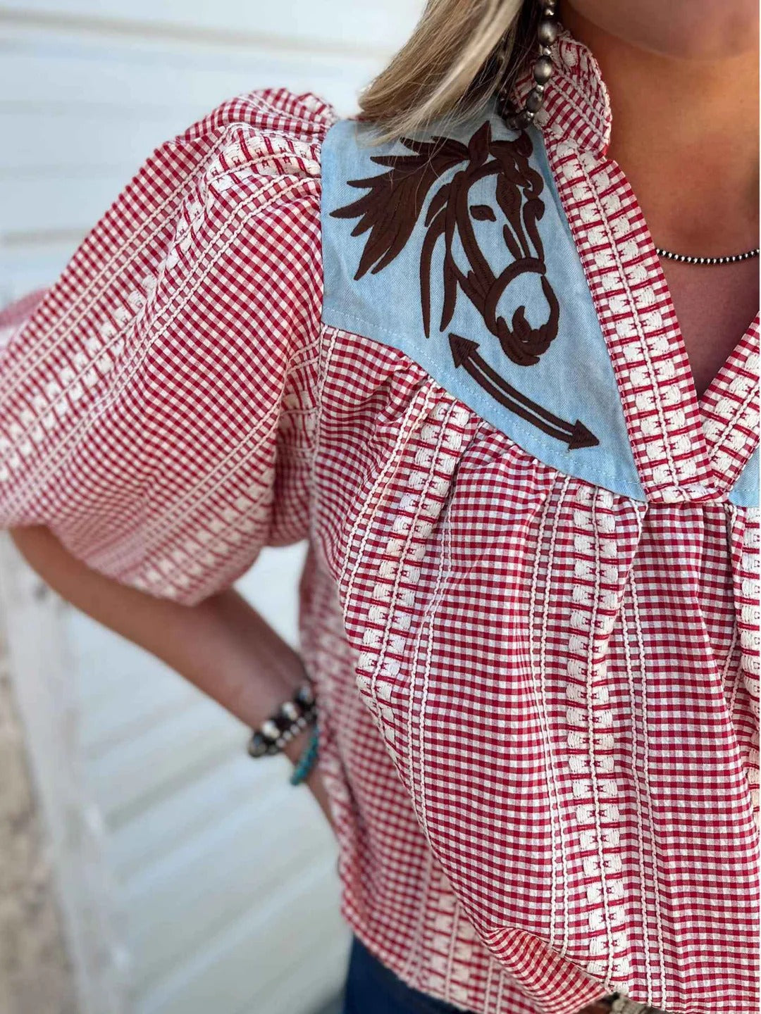Red - Women's relaxed fit blouse in a red and white gingham pattern, featuring a contrasting light blue V-neck yoke with brown embroidered horse motifs and short puff sleeves.