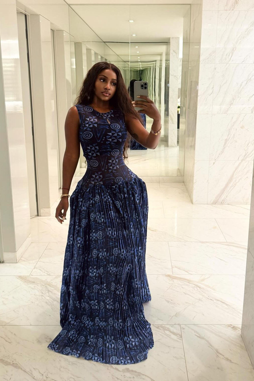 Blue - A woman wearing a sleeveless maxi dress featuring a fitted, semi-sheer geometric bodice and a voluminous gathered skirt with a mixed abstract blue print.