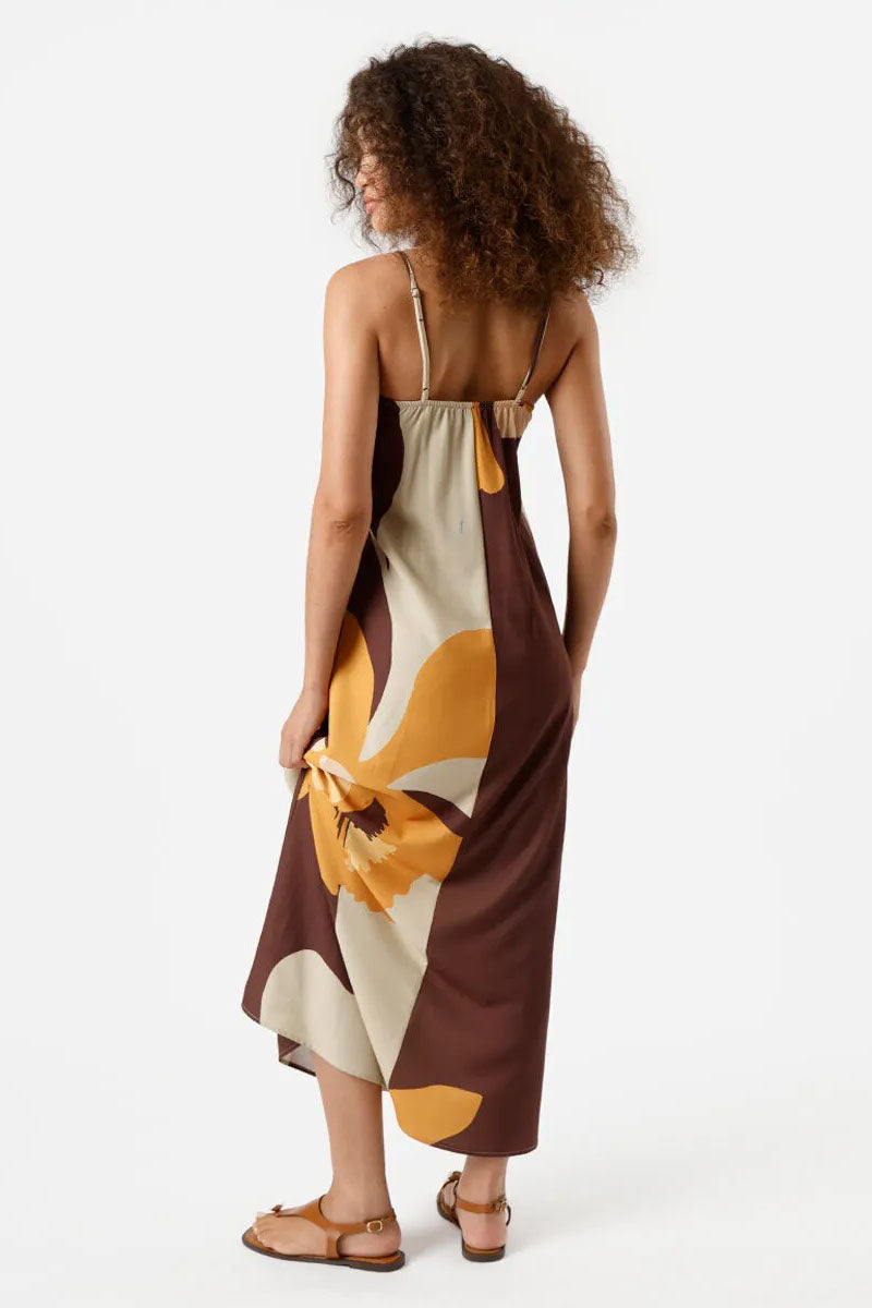 Multi - A woman wearing a long, relaxed-fit maxi dress with spaghetti straps and a fold-over straight neckline, featuring a large, bold abstract floral print in brown, mustard, and cream. She is holding a striped tote bag and wearing flat brown sandals against a white background.