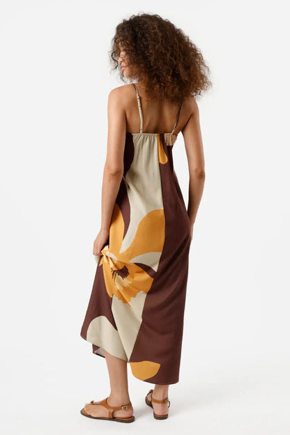Multi - A woman wearing a long, relaxed-fit maxi dress with spaghetti straps and a fold-over straight neckline, featuring a large, bold abstract floral print in brown, mustard, and cream. She is holding a striped tote bag and wearing flat brown sandals against a white background.
