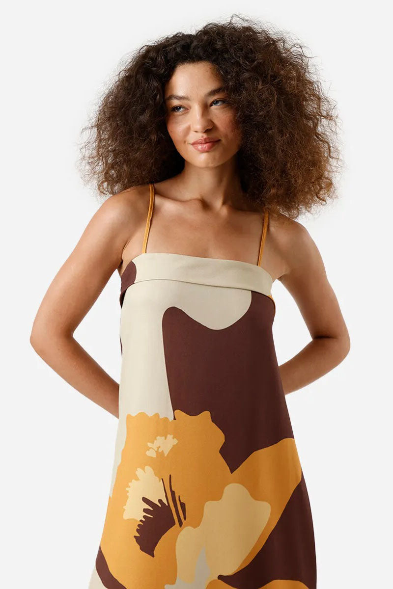 Multi - A woman wearing a long, relaxed-fit maxi dress with spaghetti straps and a fold-over straight neckline, featuring a large, bold abstract floral print in brown, mustard, and cream. She is holding a striped tote bag and wearing flat brown sandals against a white background.
