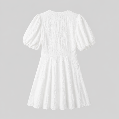 White - Woman wearing a textured jacquard A-line mini dress with a V-neckline and short puff sleeves against a grey background
