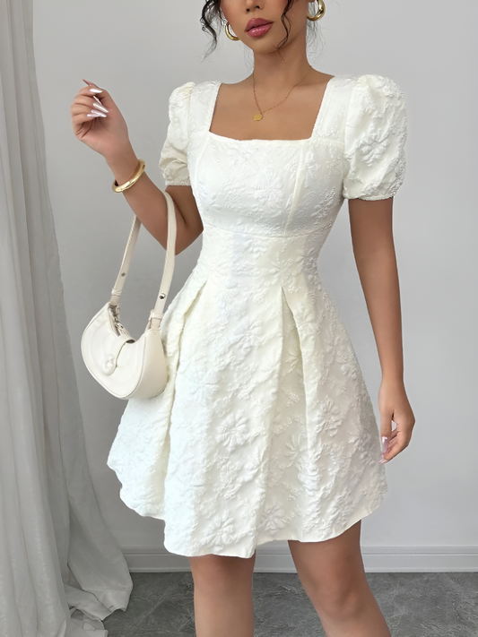 White - Model wearing a textured floral jacquard mini dress with a square neckline, short puff sleeves, and a pleated A-line skirt