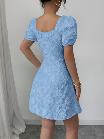 Sky Blue - Model wearing a textured floral jacquard mini dress with a square neckline, short puff sleeves, and a pleated A-line skirt