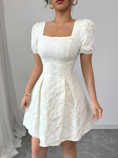 White - Model wearing a textured floral jacquard mini dress with a square neckline, short puff sleeves, and a pleated A-line skirt