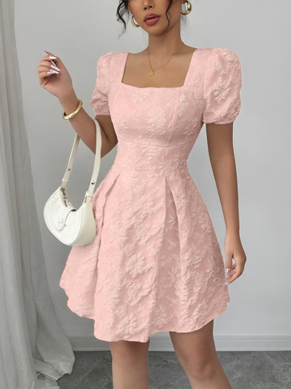 Pink - Model wearing a textured floral jacquard mini dress with a square neckline, short puff sleeves, and a pleated A-line skirt