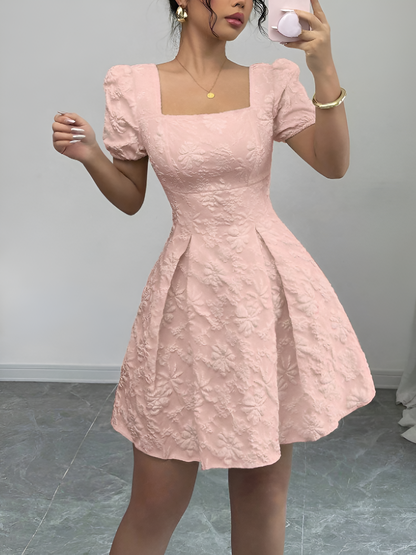 Pink - Model wearing a textured floral jacquard mini dress with a square neckline, short puff sleeves, and a pleated A-line skirt