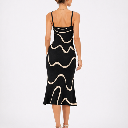 Black - Model wearing a sleeveless square-neck midi dress featuring an abstract wavy line pattern, styled with an evening clutch and heels.