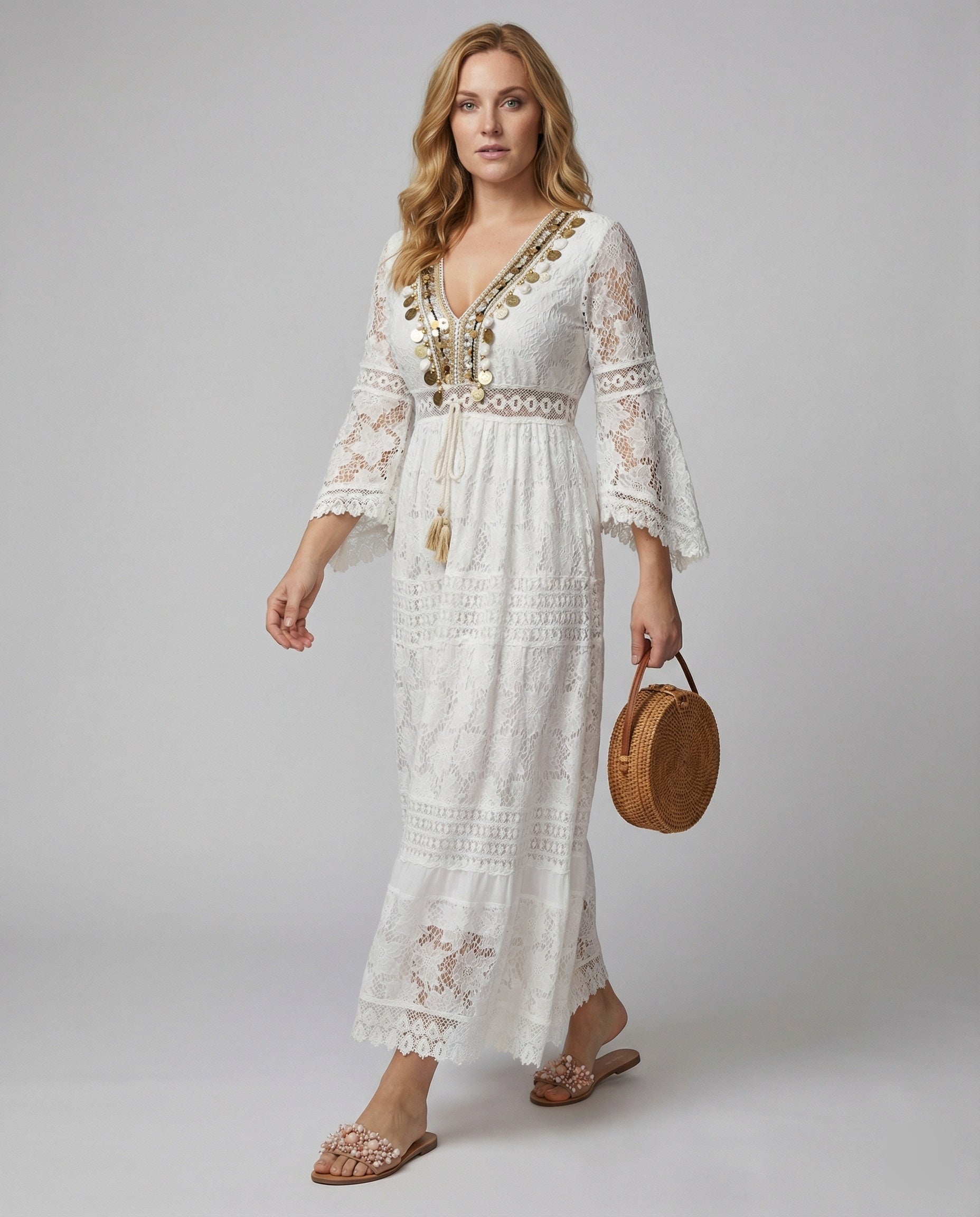 A woman wearing a bohemian lace maxi dress with a deep V-neckline, metallic embellishments, bell sleeves, and a tassel tie waist, holding a round woven bag.
