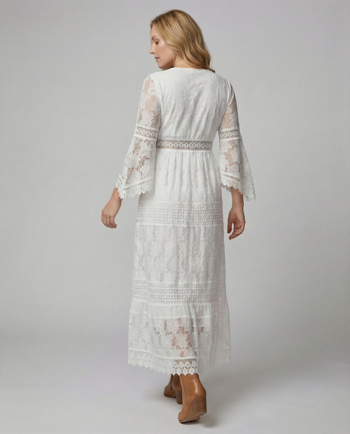 A woman wearing a bohemian lace maxi dress with a deep V-neckline, metallic embellishments, bell sleeves, and a tassel tie waist, holding a round woven bag.