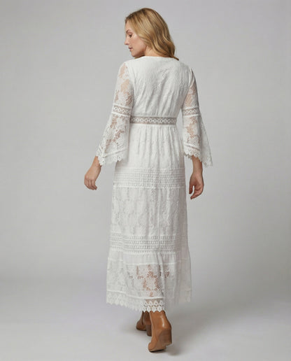 A woman wearing a bohemian lace maxi dress with a deep V-neckline, metallic embellishments, bell sleeves, and a tassel tie waist, holding a round woven bag.