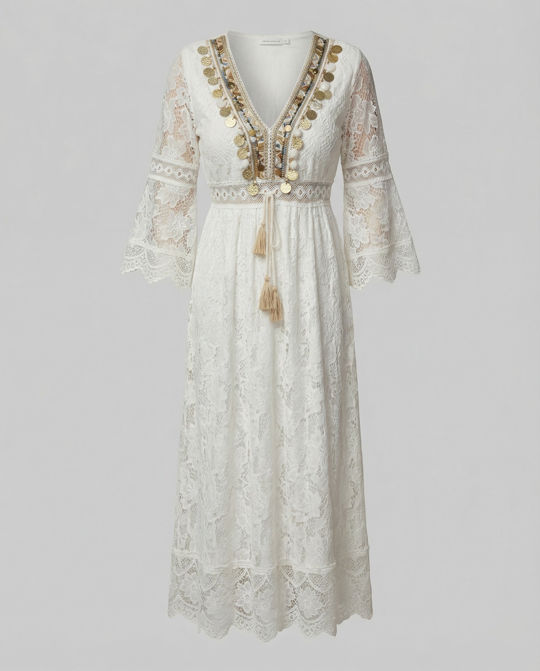 White - A woman wearing a bohemian lace maxi dress with a deep V-neckline, metallic embellishments, bell sleeves, and a tassel tie waist, holding a round woven bag.