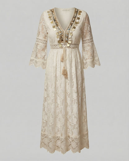 Beige - A woman wearing a bohemian lace maxi dress with a deep V-neckline, metallic embellishments, bell sleeves, and a tassel tie waist, holding a round woven bag.