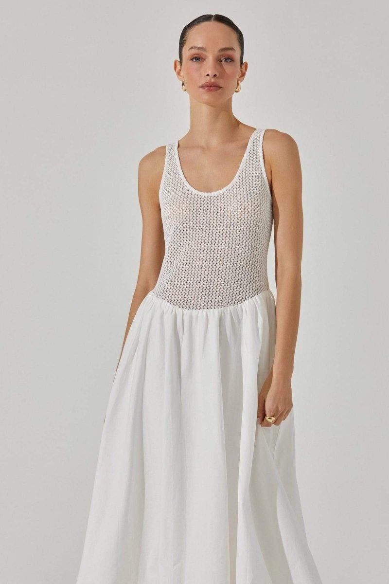 White - A woman stands against a white background wearing a sleeveless white midi dress. The dress has a textured open-knit tank-style bodice and a full, smooth A-line skirt that ends mid-calf.