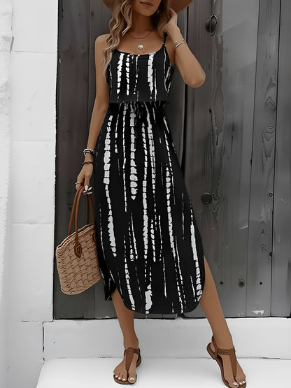 Black - Model wearing a lightweight woven strappy midi dress with an abstract vertical pattern, adjustable waist tie, and side split, standing outdoors against a white textured wall.