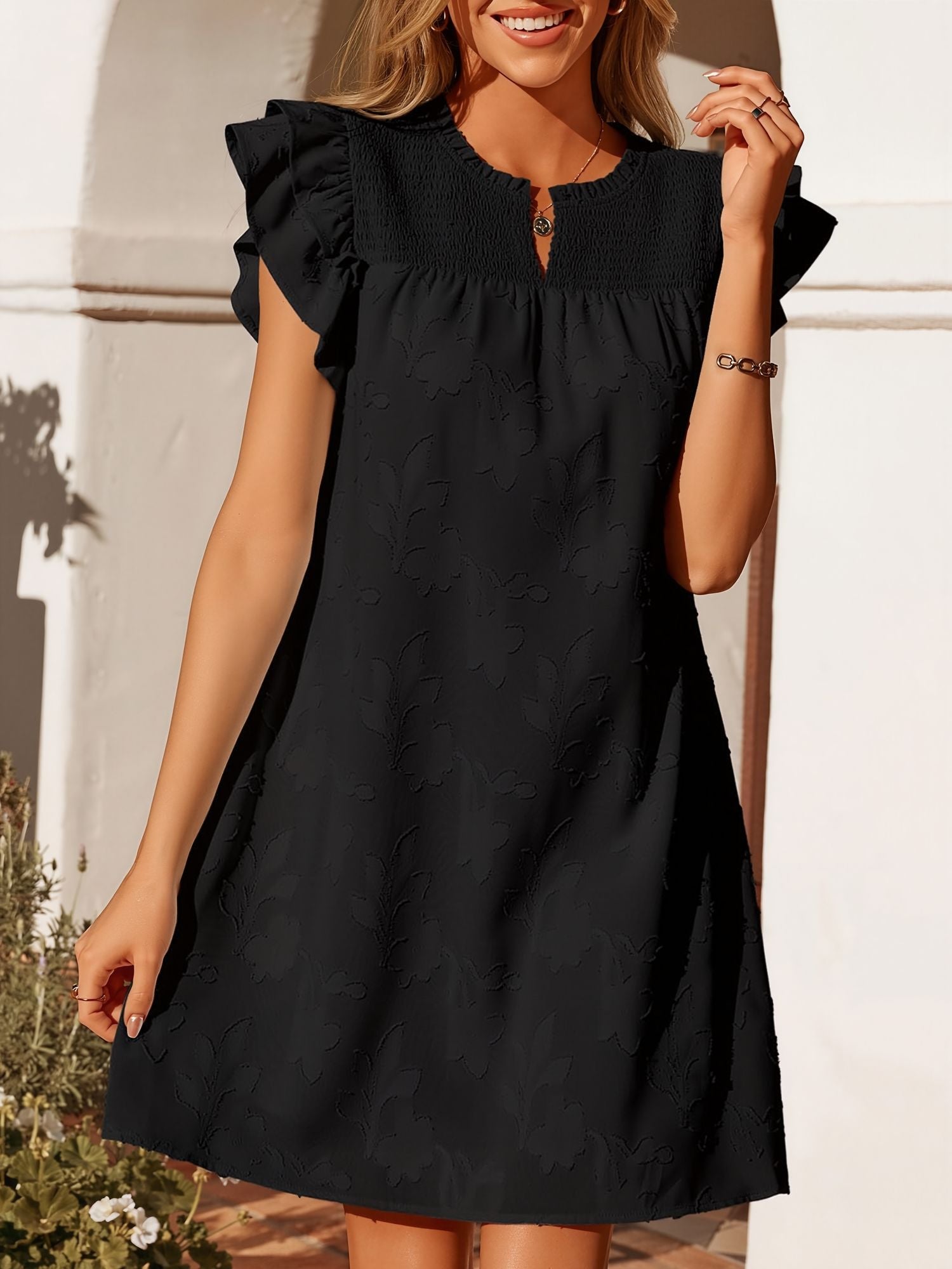 Black - Woman wearing a woven mini dress with a raised floral pattern, ruffle sleeves, and a notch neckline, standing outdoors
