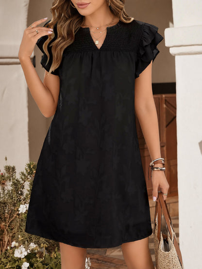 Black - Woman wearing a woven mini dress with a raised floral pattern, ruffle sleeves, and a notch neckline, standing outdoors