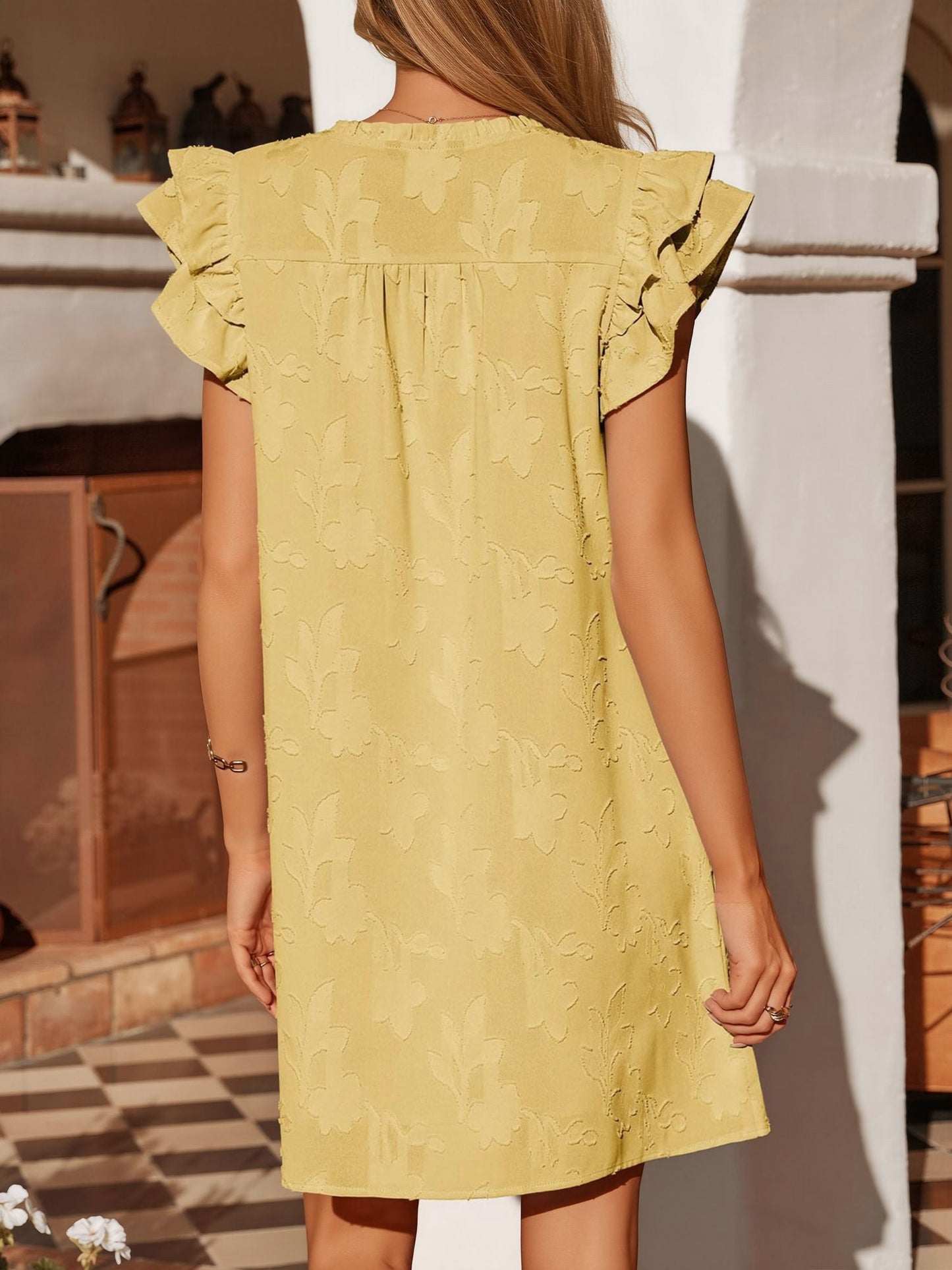 Black - Woman wearing a woven mini dress with a raised floral pattern, ruffle sleeves, and a notch neckline, standing outdoors