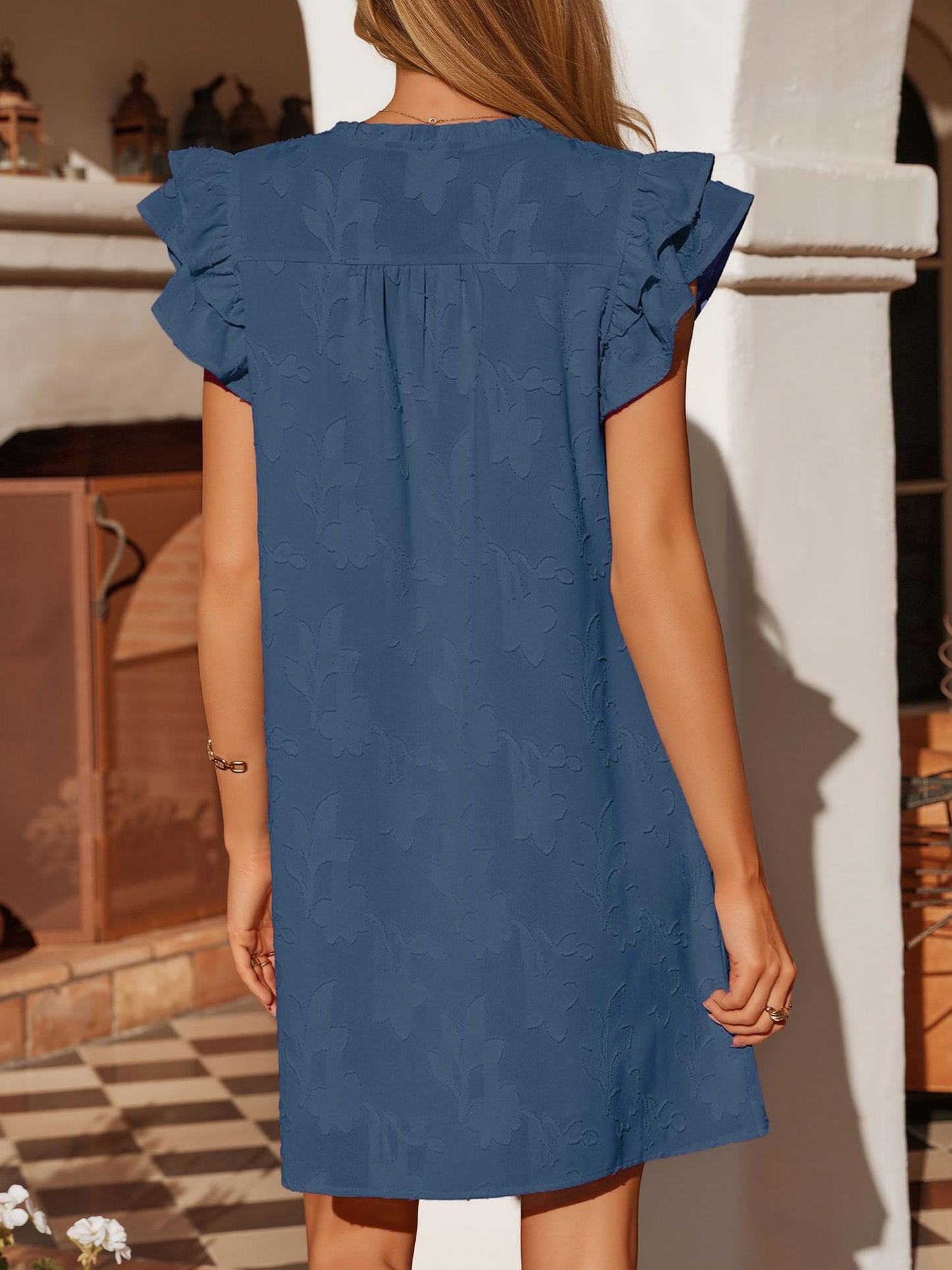 Black - Woman wearing a woven mini dress with a raised floral pattern, ruffle sleeves, and a notch neckline, standing outdoors