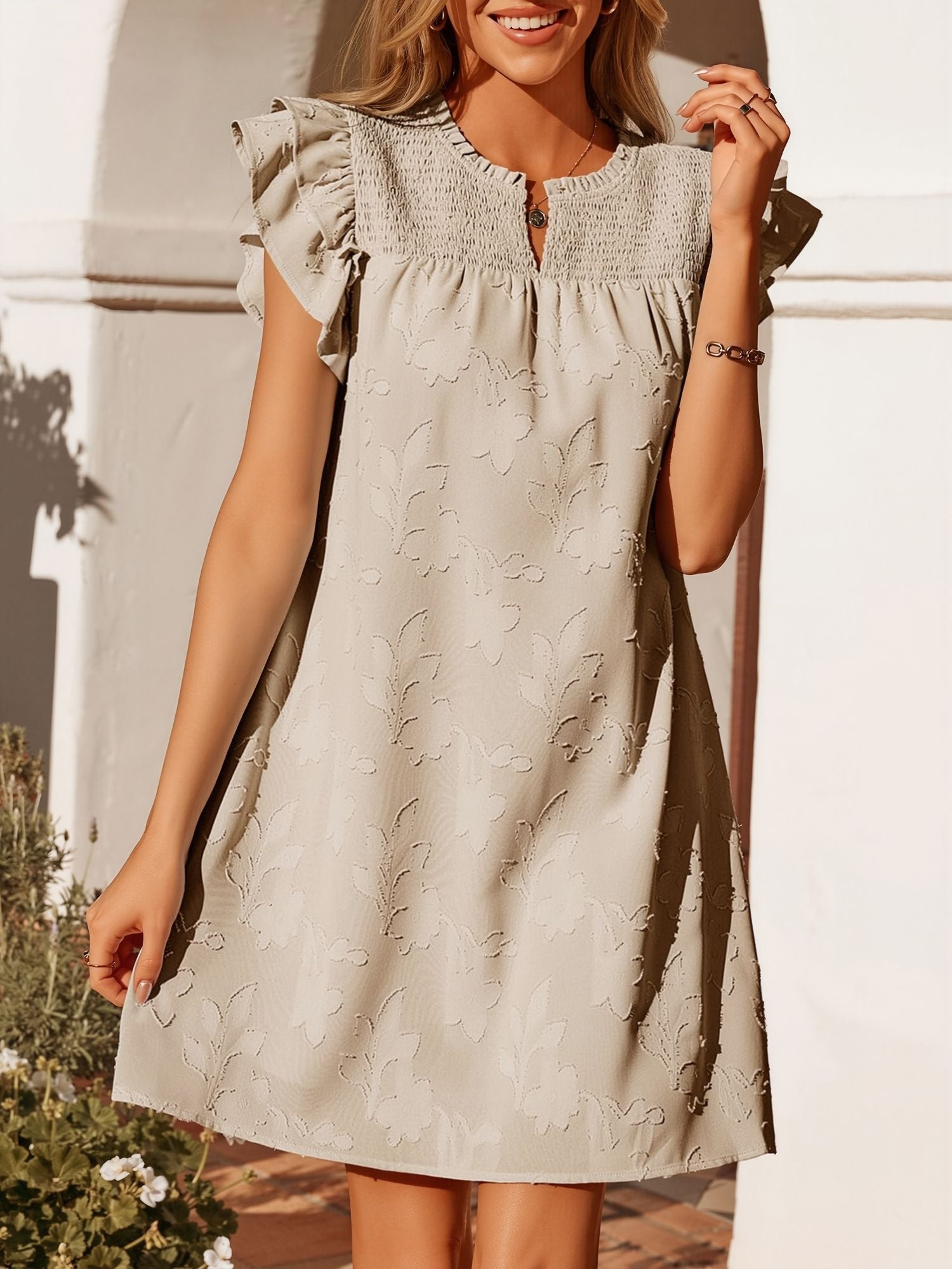 Apricot - Woman wearing a woven mini dress with a raised floral pattern, ruffle sleeves, and a notch neckline, standing outdoors