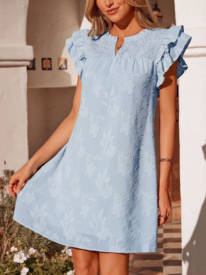 Black - Woman wearing a woven mini dress with a raised floral pattern, ruffle sleeves, and a notch neckline, standing outdoors