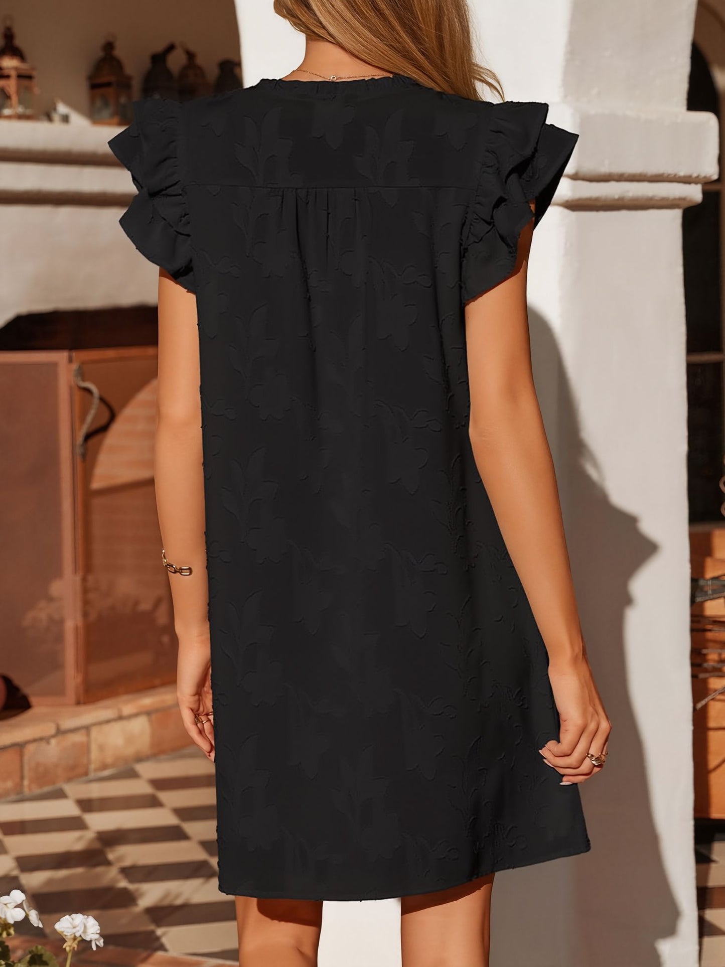 Black - Woman wearing a woven mini dress with a raised floral pattern, ruffle sleeves, and a notch neckline, standing outdoors
