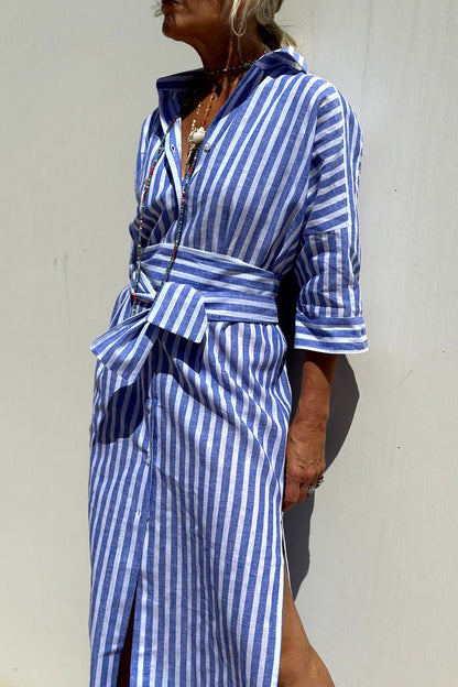 Blue - A woman wearing a striped, button-down midi-length shirt dress with 3/4 sleeves, carrying a woven straw basket bag outdoors.