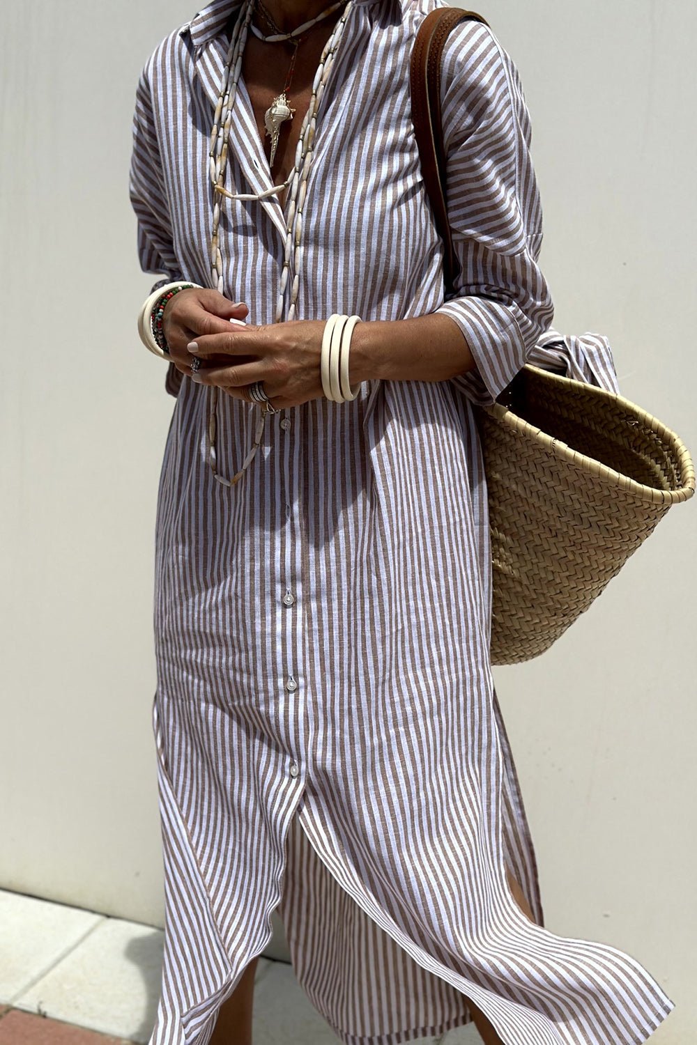 Purple - A woman wearing a striped, button-down midi-length shirt dress with 3/4 sleeves, carrying a woven straw basket bag outdoors.