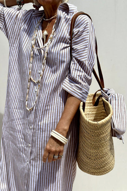 Purple - A woman wearing a striped, button-down midi-length shirt dress with 3/4 sleeves, carrying a woven straw basket bag outdoors.