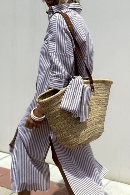 Purple - A woman wearing a striped, button-down midi-length shirt dress with 3/4 sleeves, carrying a woven straw basket bag outdoors.