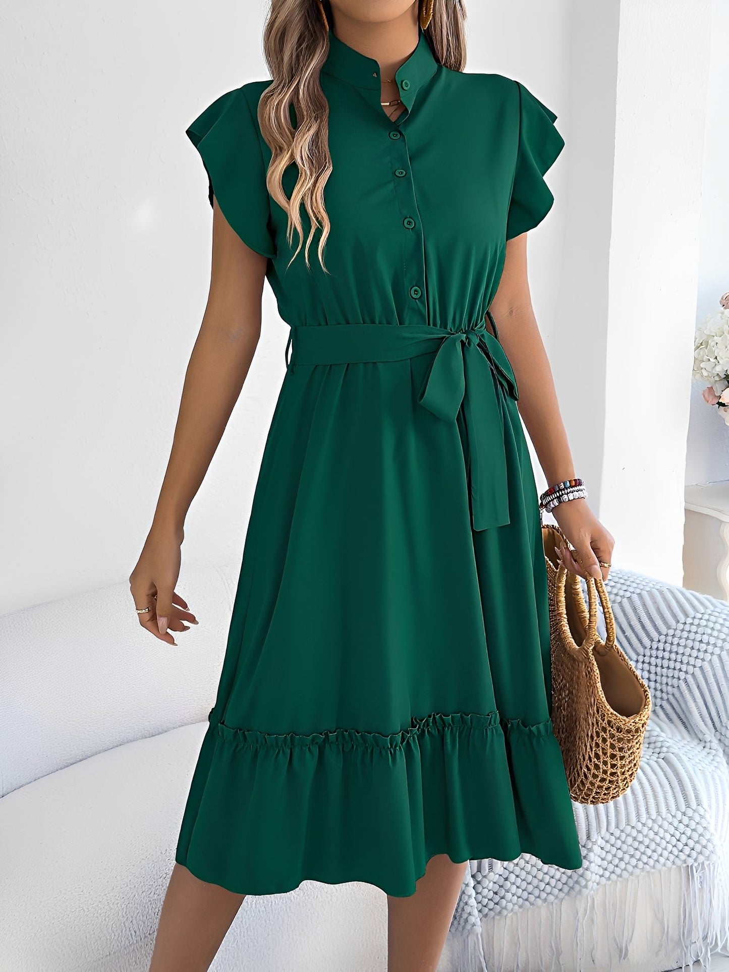 Green - A woman wearing a woven short-sleeve midi shirt dress with a collared neckline, button-down front, tie waist, and tiered ruffle hem, holding a woven bag.